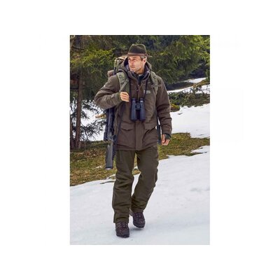 Muž v outdoorovom oblečení značky Merkel Gear kráča po zasneženej krajine. Má na sebe pánske nohavice Merkel Gear Paläarktis Gen. II, ktoré sú vetru a vodeodolné, s formovanou oblasťou kolien a vnútornými gamašmi. Na sebe má aj bundu a klobúk, nesie batoh a ďalekohľad.